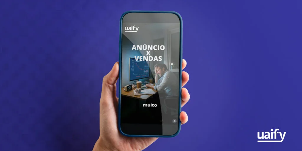 Uma mão segura um smartphone contra um fundo azul escuro. Na tela do celular, é exibido um conteúdo vertical (criativos) com o logotipo da 'uaify' no topo, o texto 'ANÚNCIO X VENDAS' em letras grandes e brancas, e a imagem de um homem estressado olhando para um gráfico com uma linha vermelha em queda no monitor do computador. A palavra 'muito' aparece na parte inferior da tela. O logotipo branco da 'uaify' também está presente no canto inferior direito do fundo da imagem principal.